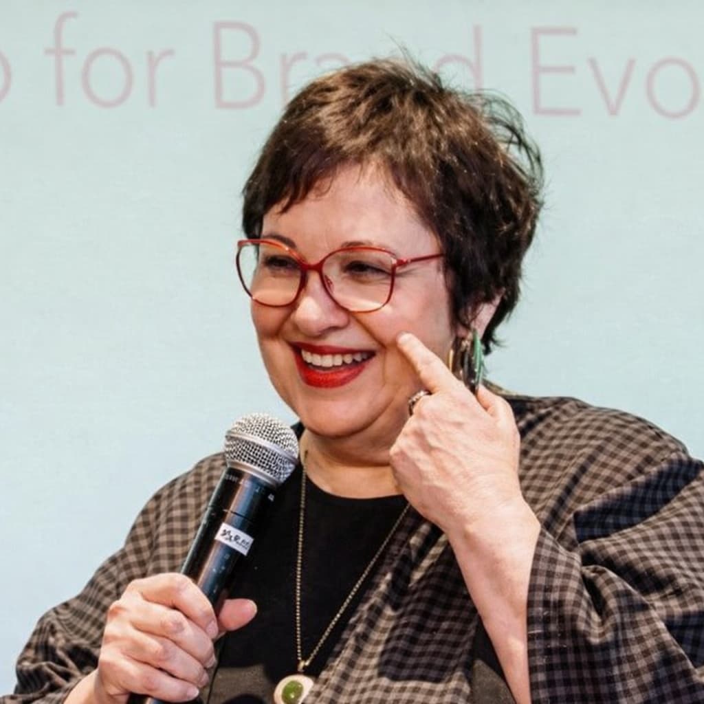 Photo of Jan Sugar at a brand event, holding a microphone and smiling.